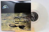 A vinyl record album with its cover jacket standing beside the translucent clear record on a small wooden stand. The cover artwork shows a dark space-like scene with a small Earth in the upper left and stylized metallic lettering across the center.