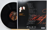A vinyl record partially pulled from its black outer sleeve, showing the back of the packaging with tracklist text, a small portrait photo, and orange script artwork on a white background.
