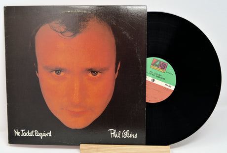 A vinyl record of Phil Collins album 'No Jacket Required' with the artist's face on the cover, placed next to a record sleeve.