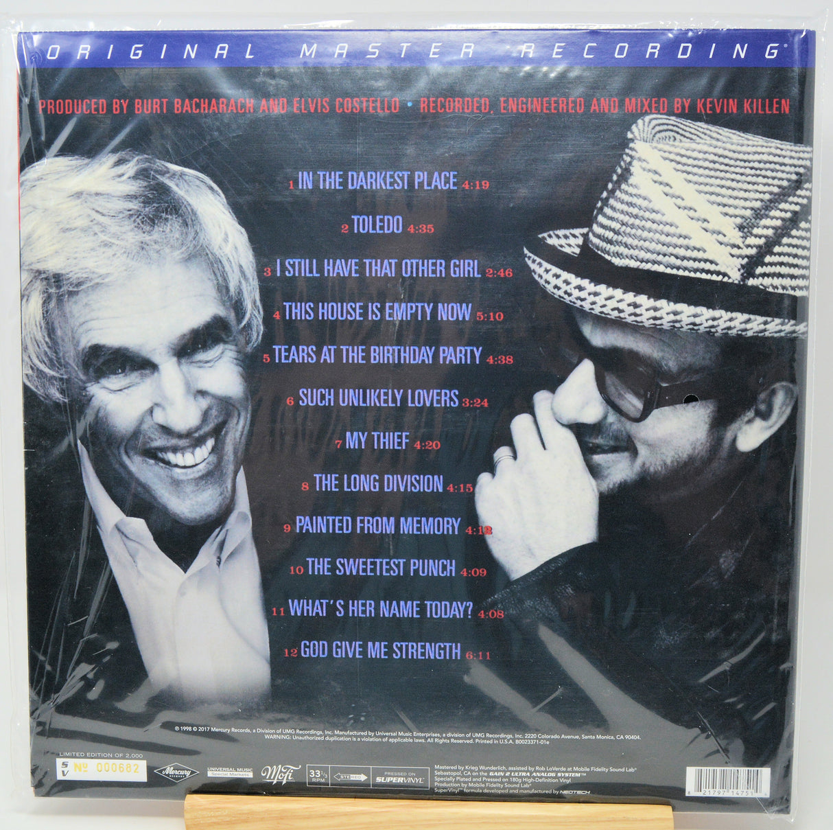 Back cover of a vinyl record sleeve for Burt Bacharach and Elvis Costello's 'Original Master Recording' album, featuring a blue header, tracklist in red and white text, and black-and-white portraits of the two artists.