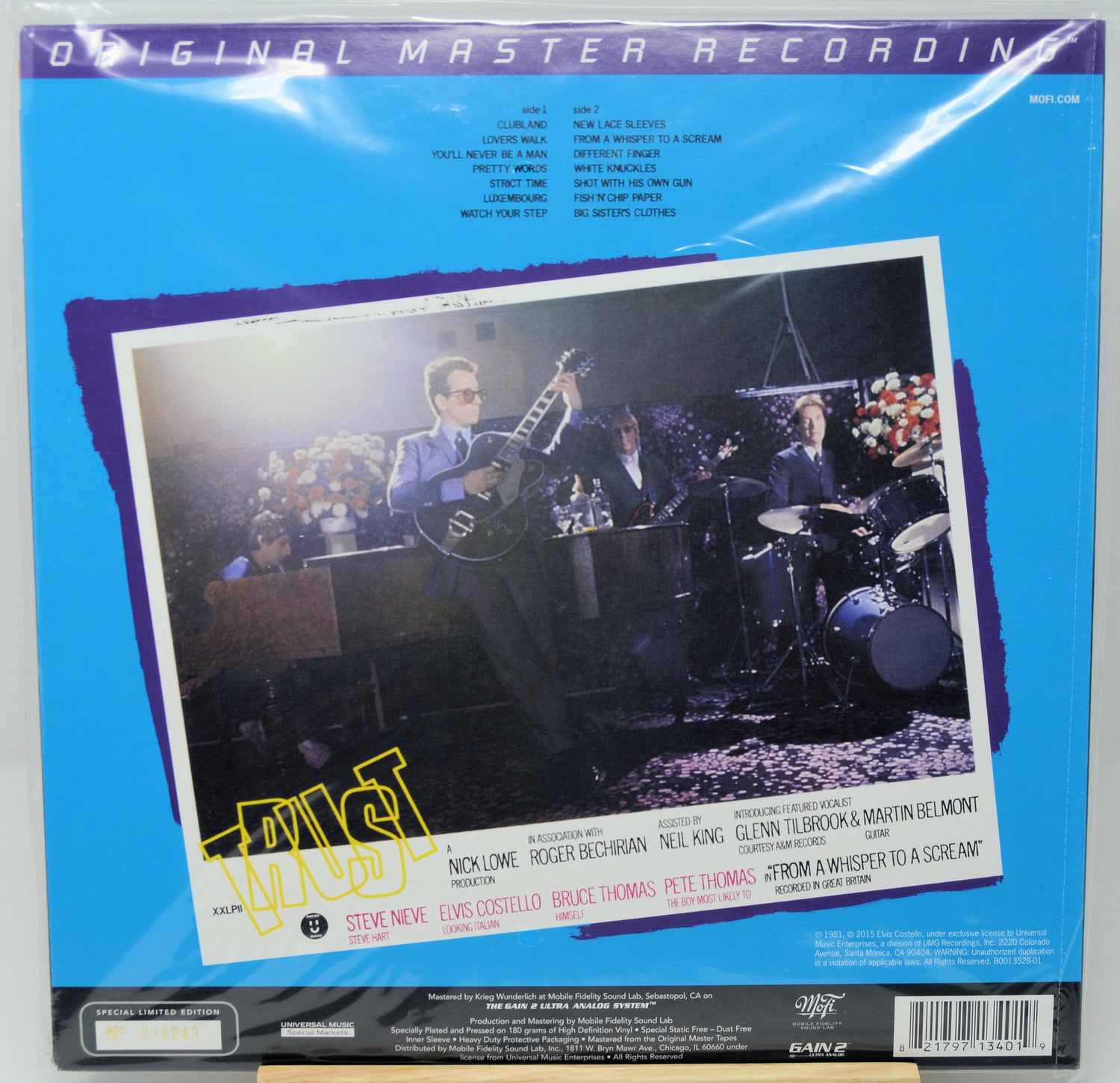 The back cover of a vinyl record sleeve for Steve Revé's album 'Must', featuring a blue background with a central photo of the band performing live on stage.