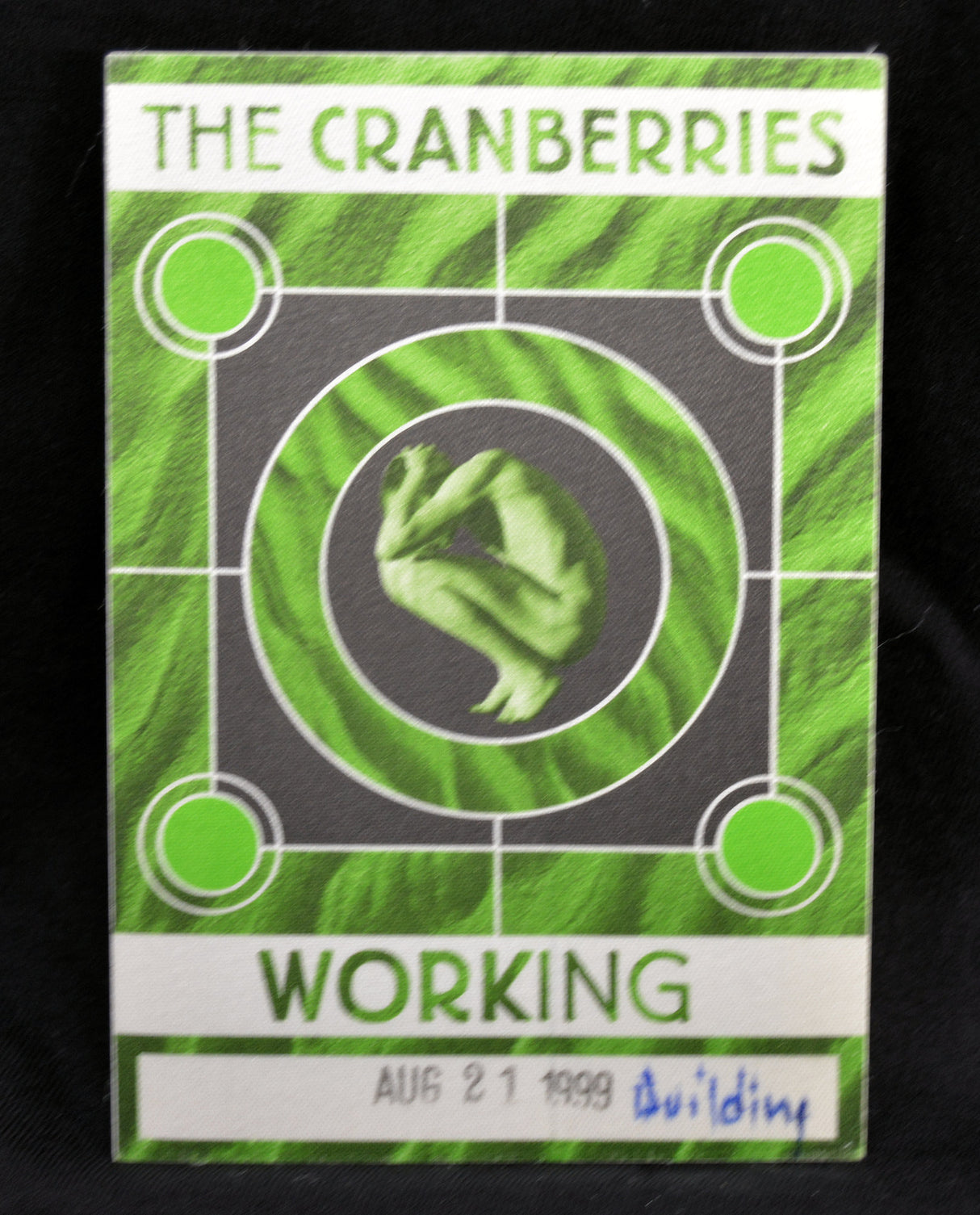 A green and white 'The Cranberries' 'Working' backstage pass from August 21, 1999, featuring the band's logo and a central green graphic, photographed against a black background.
