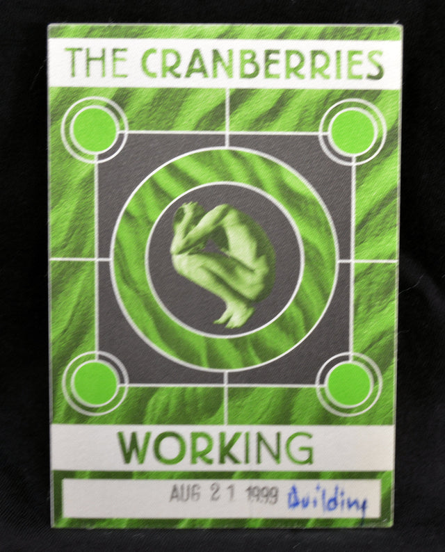 A green and white 'The Cranberries' 'Working' backstage pass from August 21, 1999, featuring the band's logo and a central green graphic, photographed against a black background.