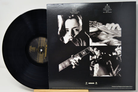 A vinyl record partially pulled from its black outer jacket, showing the back cover artwork with black-and-white photos of a musician playing guitar and text for Bob Dylan's album 'The Power and the Glory'.