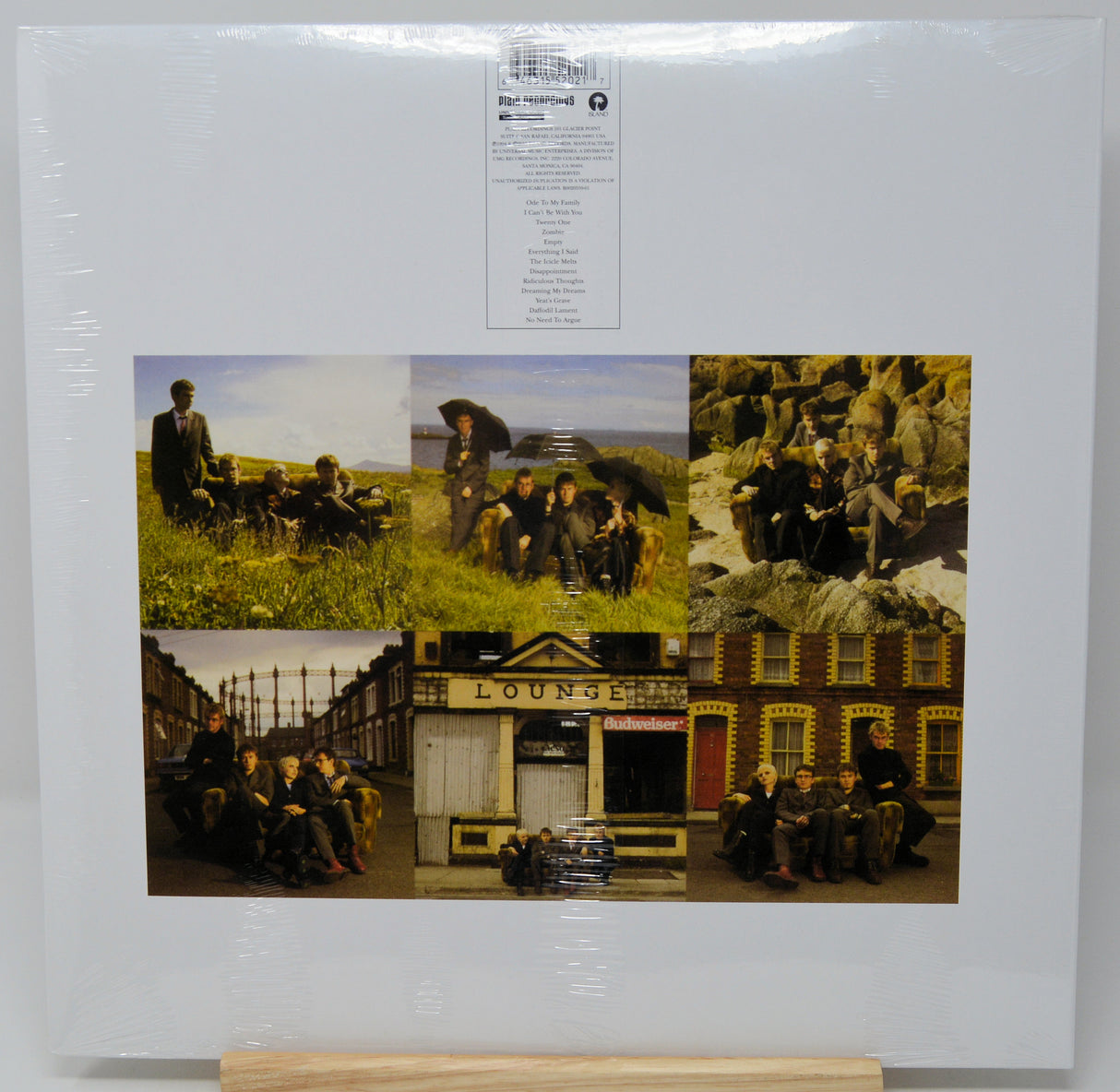 A square album cover for 'Best of Ireland 2000' by the band U2, still sealed in its original shrink wrap and displayed on a small wooden stand. The cover features a collage of six color photographs depicting the band members in various outdoor and urban settings, with a white background and a white tracklist label at the top.