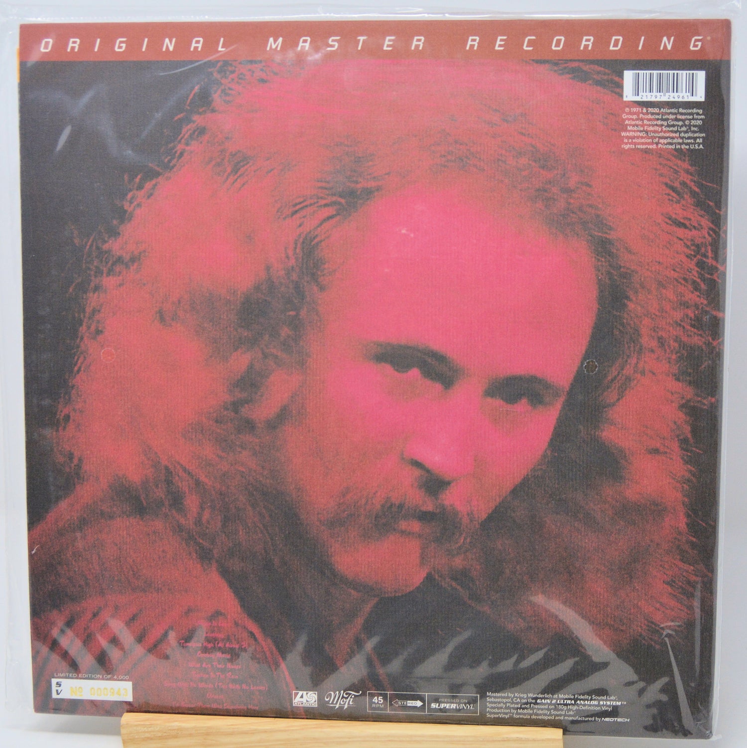 Vinyl record album cover for 'Original Master Recording' featuring a stylized portrait of a man with long hair in red and black tones, photographed in shrink wrap on a light surface.