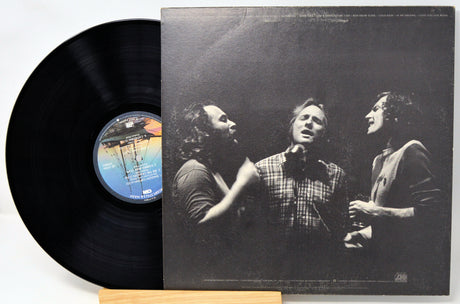 A vinyl record partially pulled from its black-and-white album cover, displayed on a small wooden stand against a plain light background.