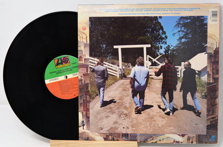 Vinyl record with a cover showing four people walking towards a wooden gate.