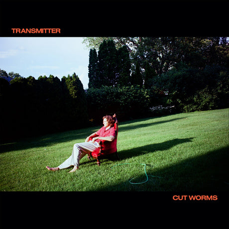 Person sitting on a red chair in a grassy field with trees in the background, album cover for 'Transmitter' by Cut Worms.