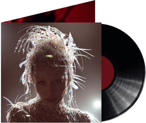 A vinyl record with Miley Cyrus on the cover, artistically dressed with a floral-like arrangement on her head, releasing from a red record sleeve.