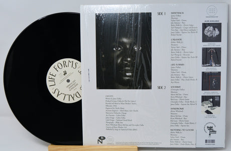 Vinyl record with cover displaying tracklist and album art on a light gray background