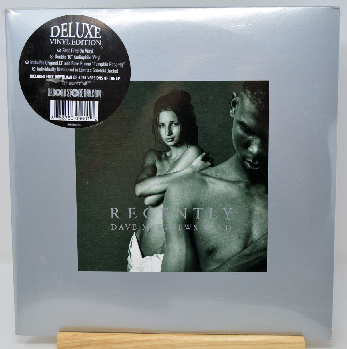 Dave Matthews and Linda 'Recently' Deluxe Vinyl Edition LP cover, sealed in its original plastic shrink wrap and standing on a light wood block. The cover is a muted gray-green with a black circular sticker on the top left.