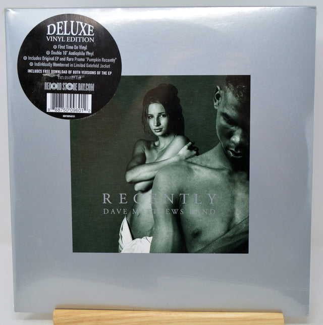 Dave Matthews and Linda 'Recently' Deluxe Vinyl Edition LP cover, sealed in its original plastic shrink wrap and standing on a light wood block. The cover is a muted gray-green with a black circular sticker on the top left.