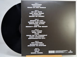 The back of a vinyl record sleeve displayed on a small wooden stand, showing the tracklist in white text on a black background with part of the black record visible at the left edge.