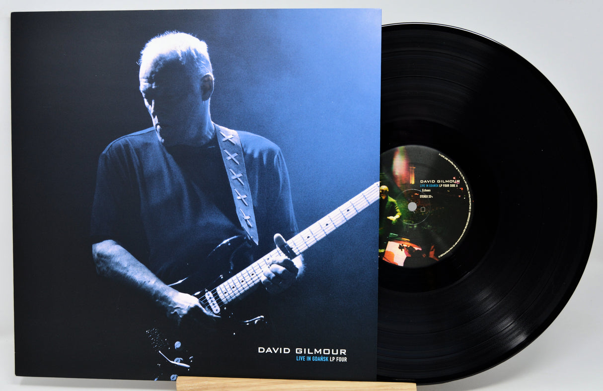 David Gilmour 'Live in London 1974' vinyl record LP with its illustrated cover jacket standing next to the black vinyl disc on a small wooden stand.