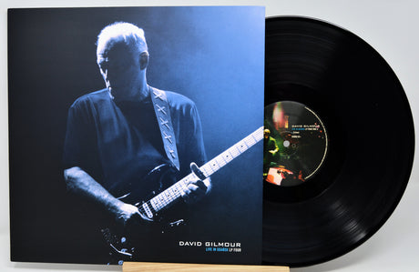 David Gilmour 'Live in London 1974' vinyl record LP with its illustrated cover jacket standing next to the black vinyl disc on a small wooden stand.