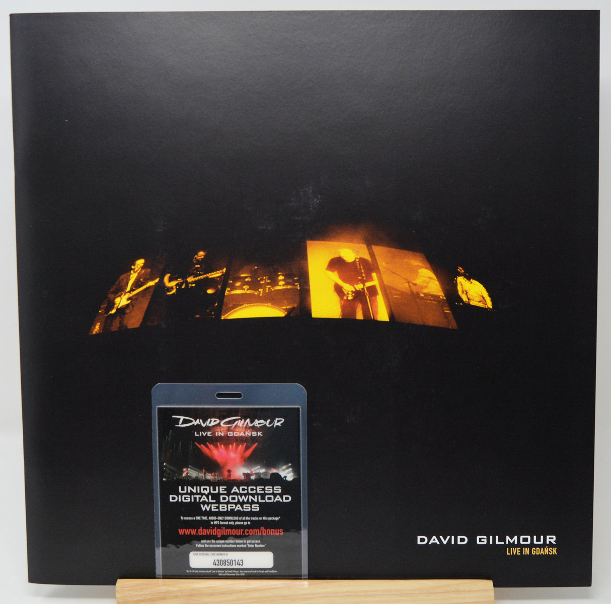 David Gilmour 'Live in Berlin' album cover displayed upright, featuring a black background with a row of warm orange stage-light panels across the center and a small digital download webpass card in front.