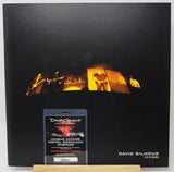 David Gilmour 'Live in Berlin' album cover displayed upright, featuring a black background with a row of warm orange stage-light panels across the center and a small digital download webpass card in front.