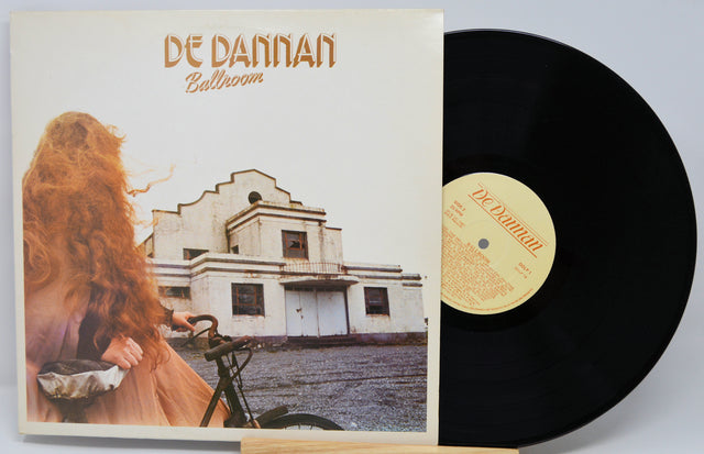 Vinyl record with cover featuring a person with long hair and a bicycle, set against an old building.