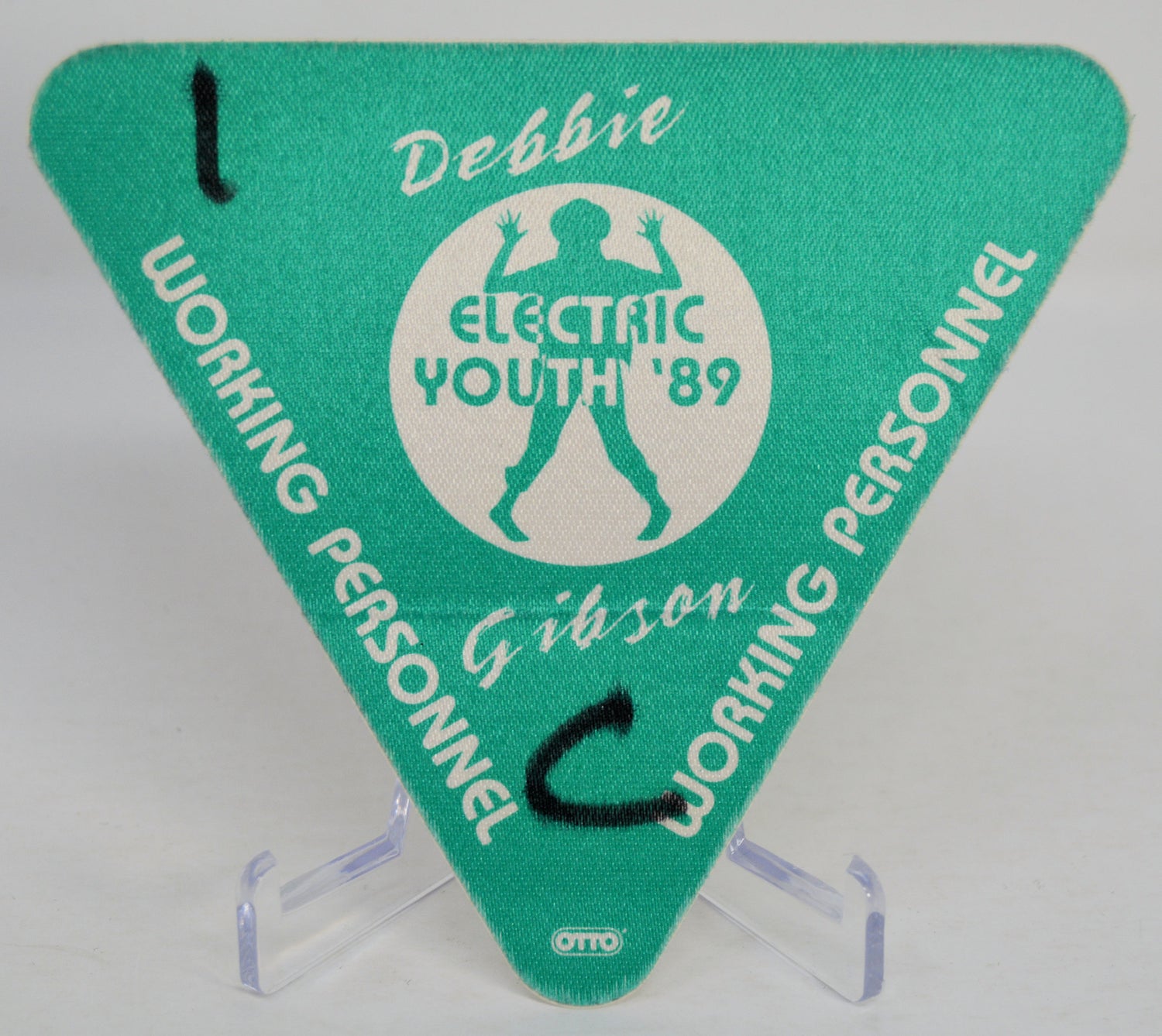 Green triangle-shaped backstage pass with 'Debbie Gibson Electric Youth '89' design on a clear stand.