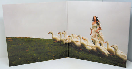 Gatefold artwork of Deeper Well album featuring a woman in a floral dress walking with white ducks on a grassy hill