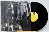 Vinyl record with a black and white album cover showing a group of people in a room.
