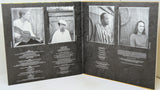An open book or album booklet with four black-and-white portrait photos across the spread and blocks of small white text below each photo, photographed against a light neutral background.