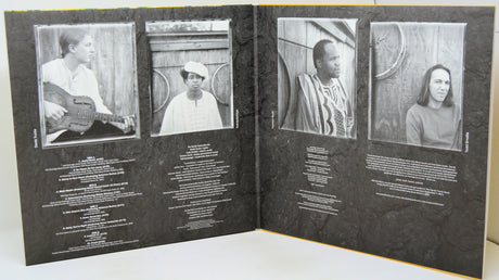 An open book or album booklet with four black-and-white portrait photos across the spread and blocks of small white text below each photo, photographed against a light neutral background.