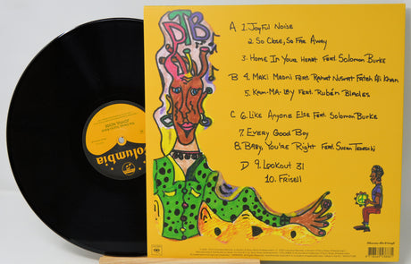A vinyl record partially pulled from its sleeve, showing the black Columbia LP disc and the yellow album cover with a colorful illustrated portrait and printed tracklist.