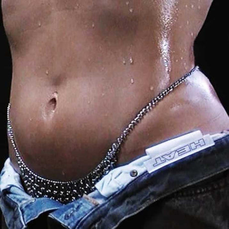 Close-up of glistening torso with chain and HEAT label on denim