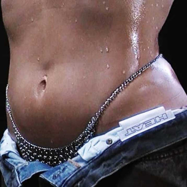 Close-up of glistening torso with chain and HEAT label on denim