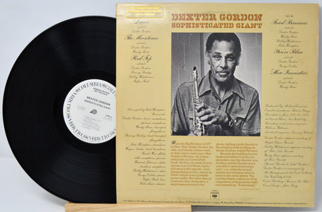 A vinyl record and its album cover for Deeter Gordon's 'Sophisticated Giant' are displayed side by side on a light wood surface. The cover is cream-colored with a black-and-white portrait of the artist holding a saxophone, and the black vinyl record is partially visible on the left.