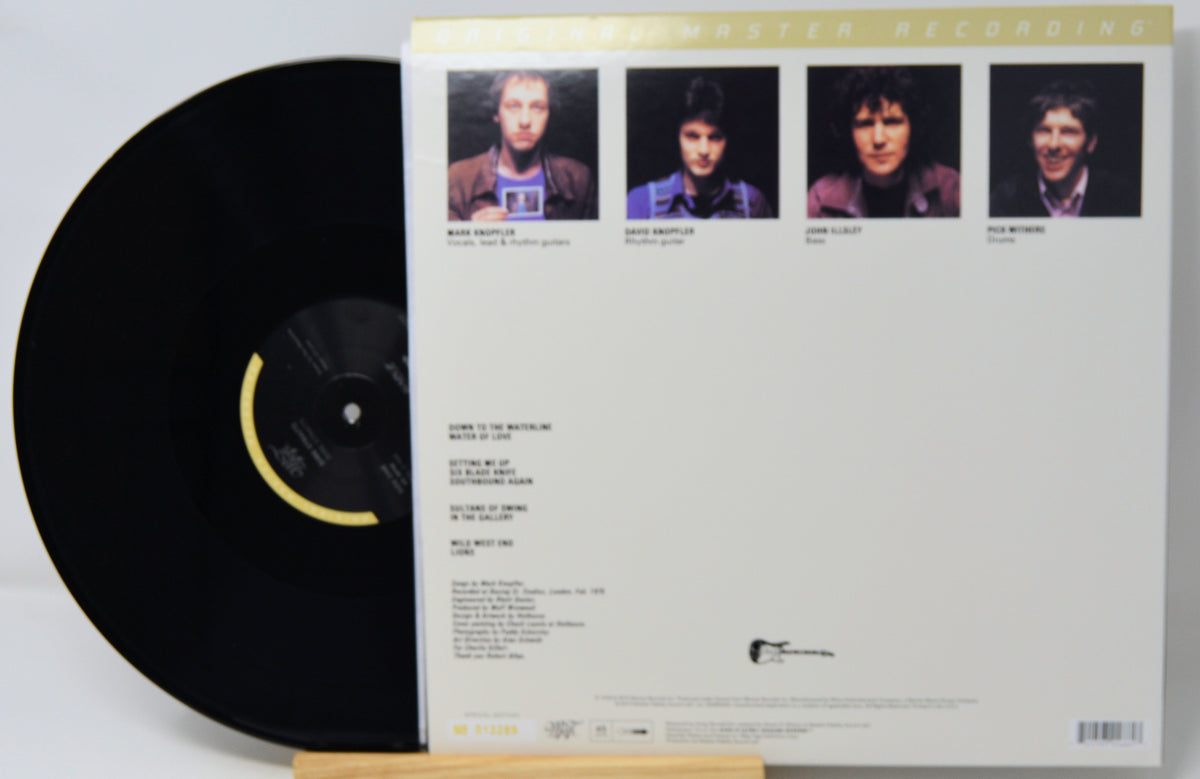 A vinyl record partially pulled from its sleeve, showing the back of the album cover with four portrait photos at the top and track listing text below, displayed on a small wooden stand.
