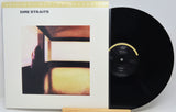 Dire Straits 'Live at Leeds' vinyl record shown with its album cover sleeve and a black LP partially pulled out, displayed on a small wooden stand against a light gray background.
