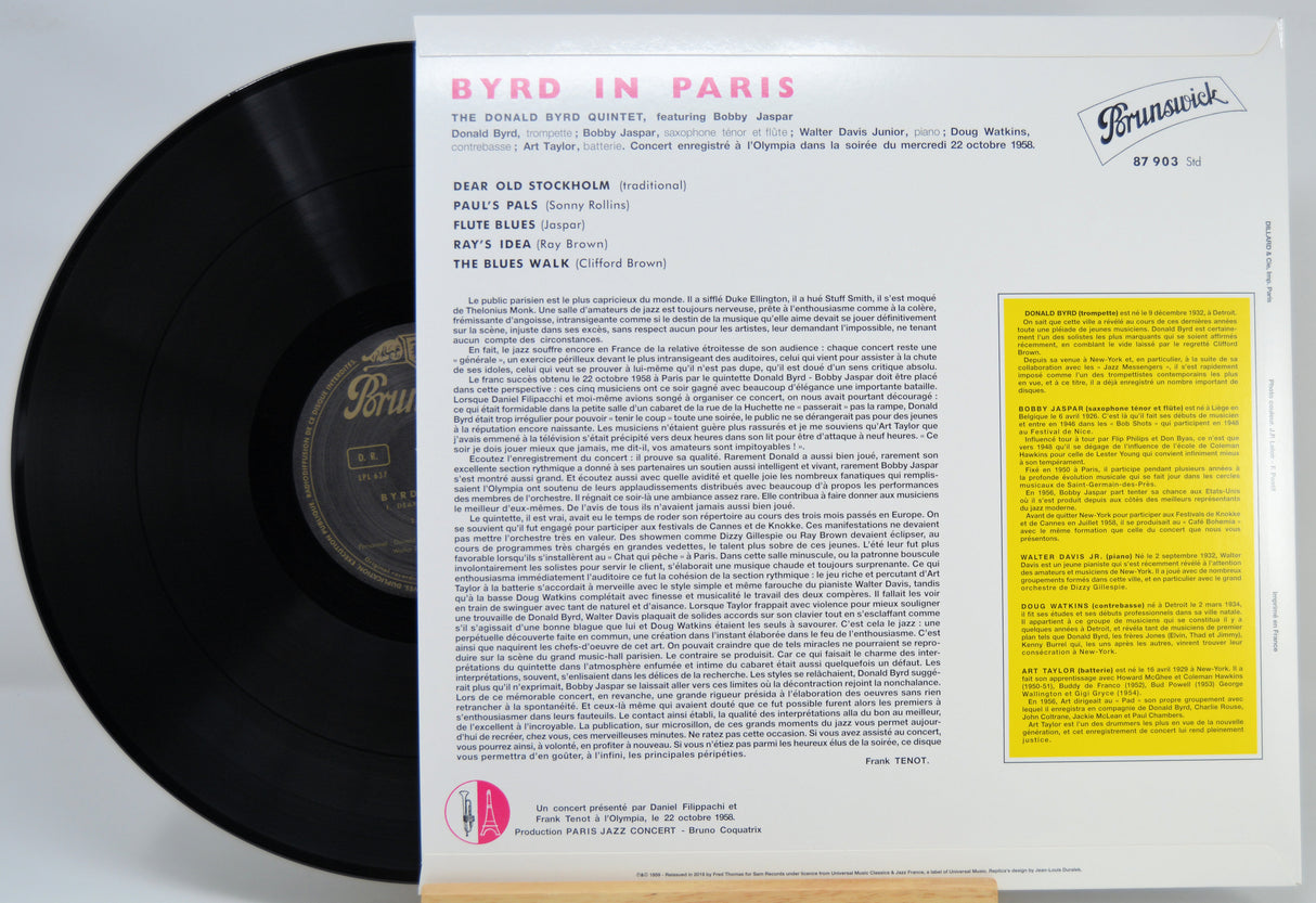 Vinyl record sleeve and black record partially pulled from the inner paper sleeve for Byrd in Paris, with printed tracklist text and a yellow information panel on a white background.