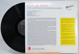 Vinyl record sleeve and black record partially pulled from the inner paper sleeve for Byrd in Paris, with printed tracklist text and a yellow information panel on a white background.