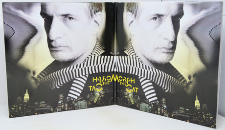 A folded book or album cover featuring a black-and-white portrait of a man wearing a striped shirt, with a city skyline at the bottom and the title 'How to Become the Cat' in yellow text.