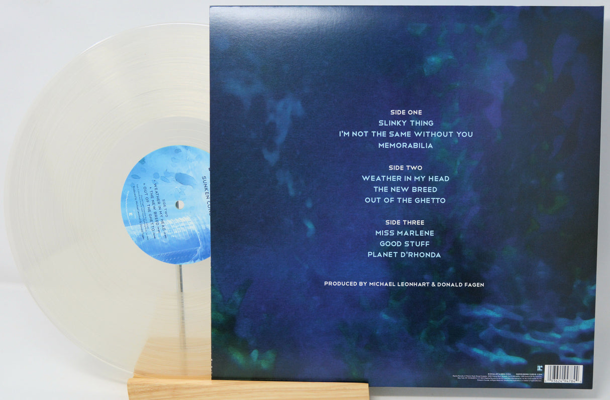 Vinyl record album shown with the back cover standing upright and part of the translucent clear record resting beside it on a small wooden stand.