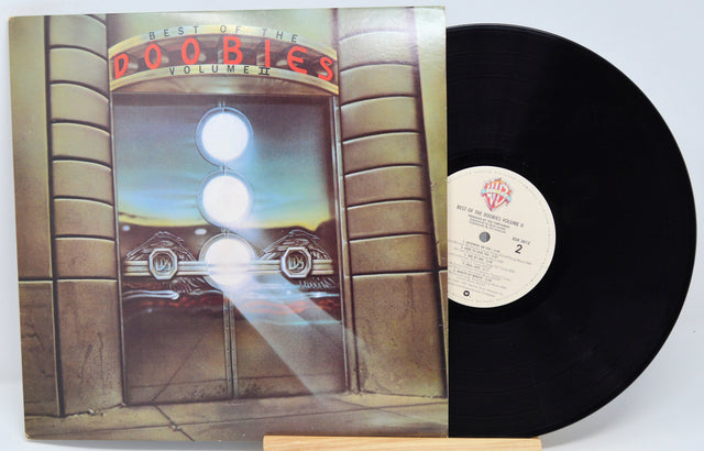 A vinyl record of The Doobie Brothers - Best Of Vol 2 with a sleeve featuring a neon-lit storefront and the band's name.