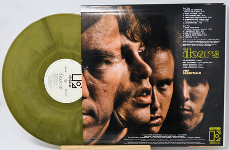 A green translucent vinyl record partially visible behind the back cover of a The Doors 'Essentials' LP, showing the tracklist and front cover artwork on a white background.