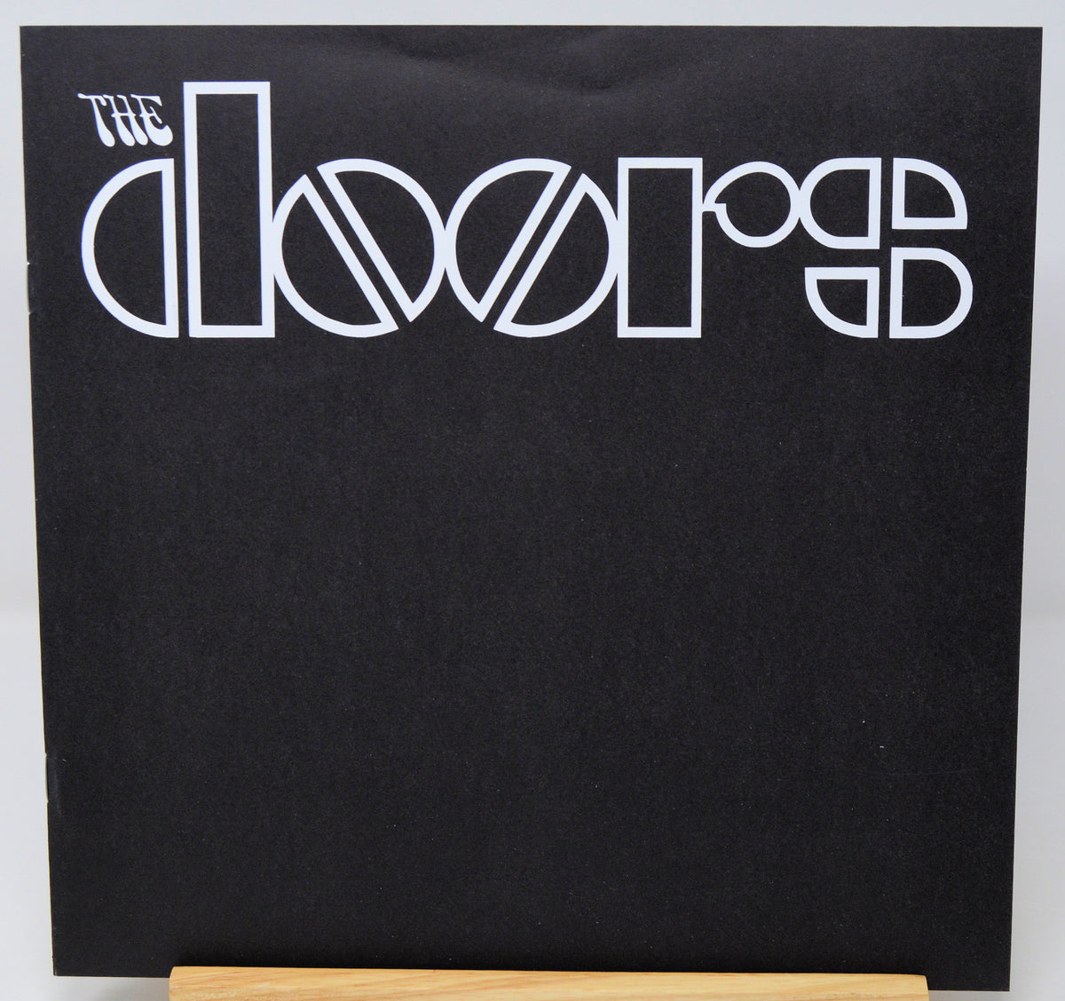 The Doors 'Rumours' vinyl record album cover, featuring the band's name in white stylized lettering on a black background, displayed on a wooden stand.
