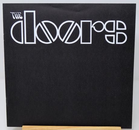 The Doors 'Rumours' vinyl record album cover, featuring the band's name in white stylized lettering on a black background, displayed on a wooden stand.