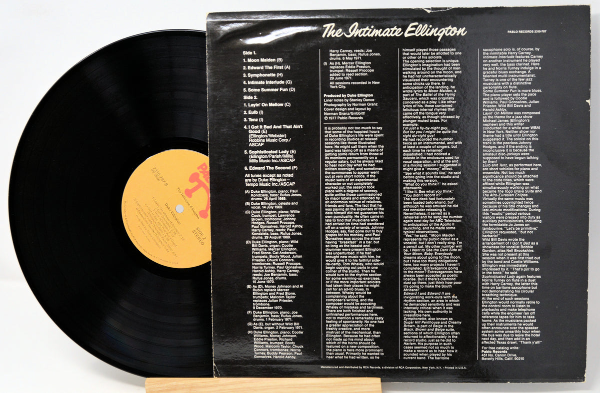A vinyl record partially pulled from its black outer sleeve, showing the back cover track listing and the black record with a yellow label on a white background.