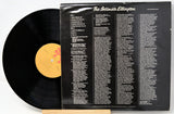A vinyl record partially pulled from its black outer sleeve, showing the back cover track listing and the black record with a yellow label on a white background.