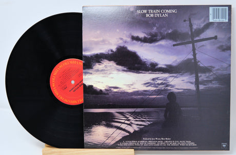 Vinyl record and back cover for Bob Dylan titled 'Slow Train Coming' showing someone sitting in a boat on the ocean at dusk.