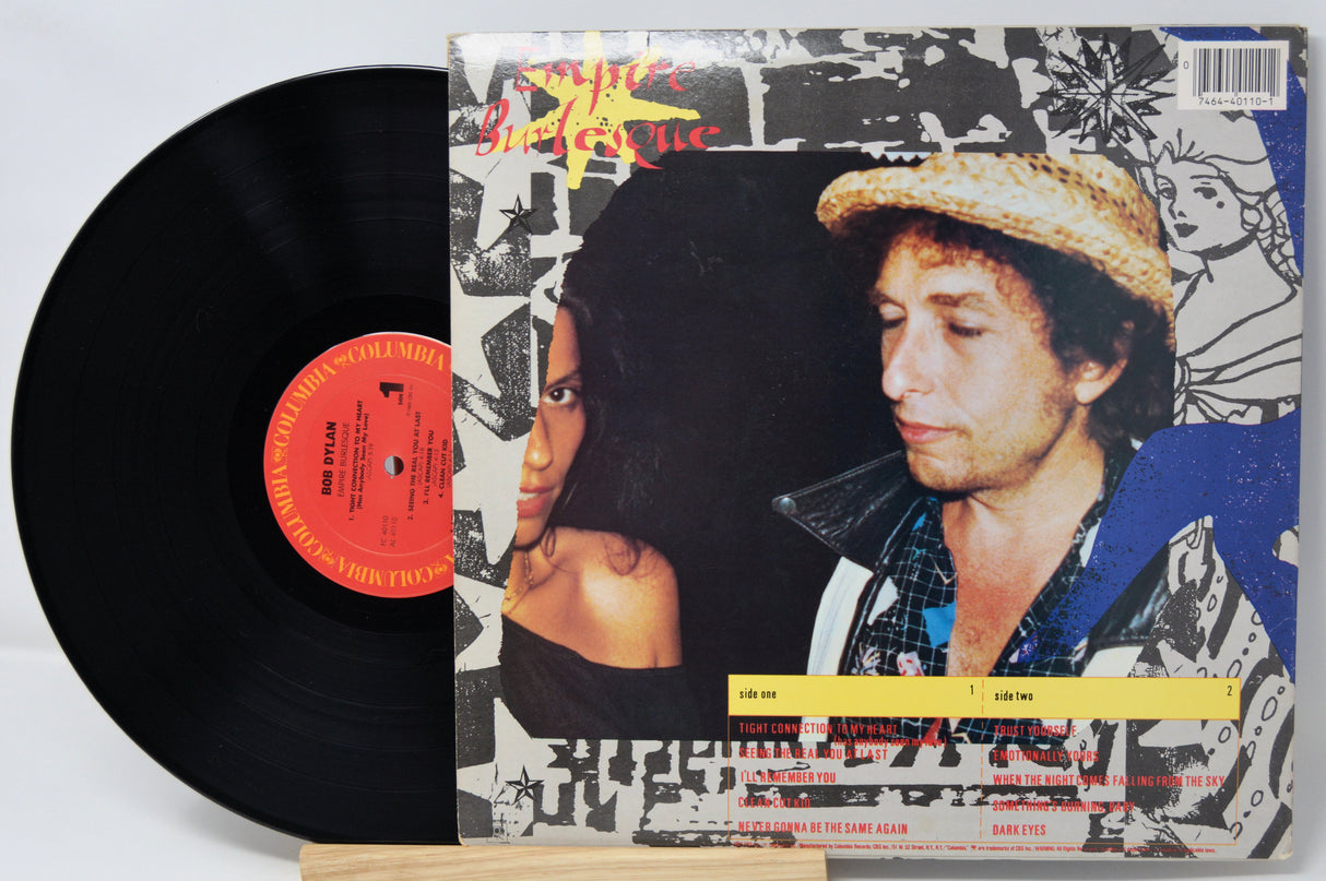 Vinyl record with a colorful cover featuring two people, on a light gray background.