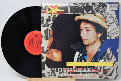 Vinyl record with a colorful cover featuring two people, on a light gray background.