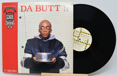 A 12-inch vinyl single record partially pulled from its sleeve, featuring the artist Da Butt. The album cover has a red side panel, lined paper background, and a photo of the artist holding a sign that reads 'DOG OR DAY'.