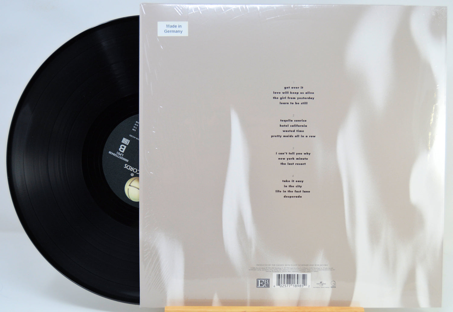 A vinyl record partially pulled from its sleeve, showing the back of the album packaging with printed track listing and barcode on a white background.