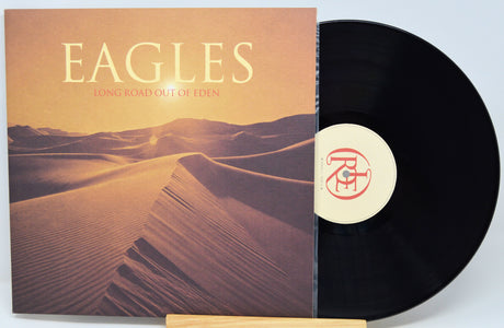 Eagles - Long Road Out of Eden vinyl record LP with the album cover sleeve and a black vinyl disc partially visible, displayed on a small wooden stand against a light gray background.